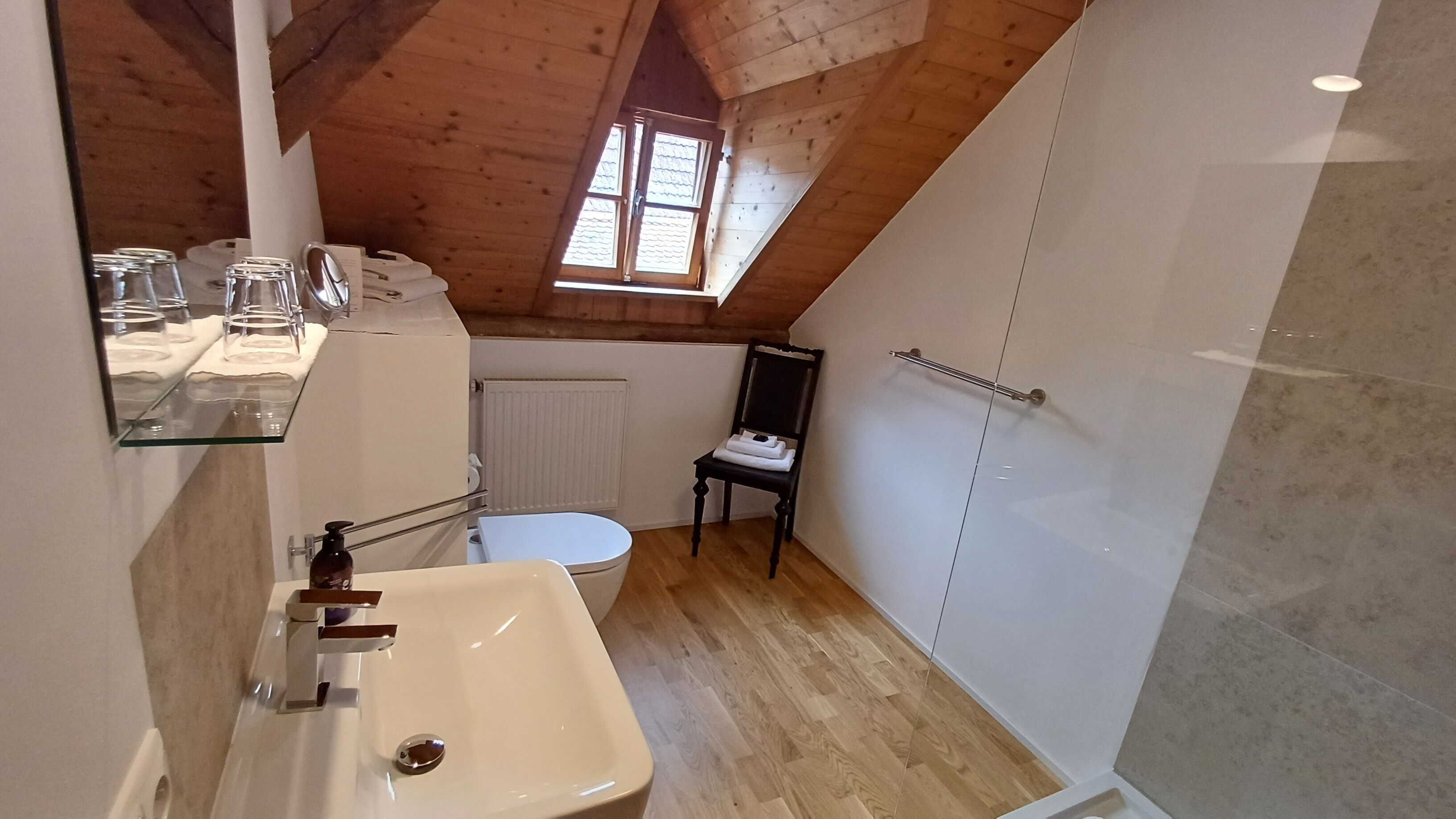 A small, modern bathroom with a wooden ceiling, a white sink, a toilet, and a small window.