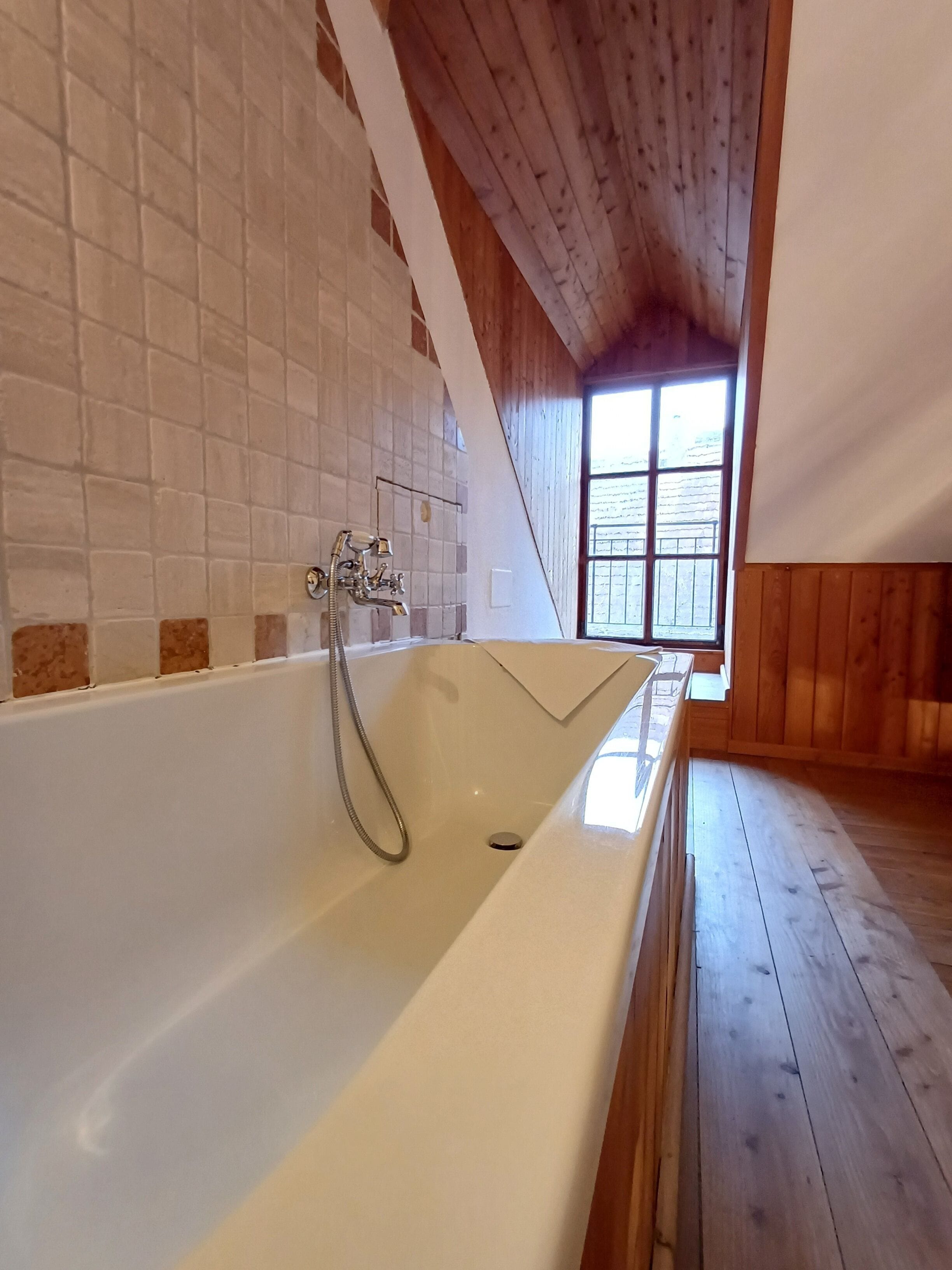 A large bathtub with a showerhead, wooden walls, and a window in the background.