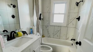 Et lille badeværelse med et hvidt håndvask, toilet og badekar.
