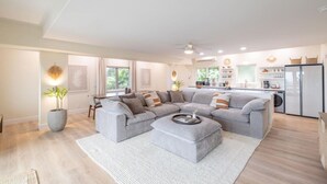 A spacious living room with a grey sectional sofa, a dining area, and a kitchen with modern appliances. - Kona Sunset Retreat | Walk to Shops & Dining (Kailua-Kona)