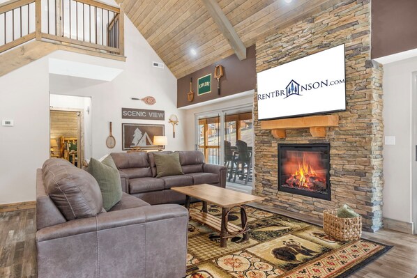 A spacious living room with a stone fireplace, leather sofa, and a view of the outside.