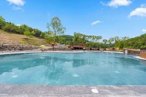 Una piscina cristalina con sillas de descanso y sombrillas, rodeada de edificios y árboles.