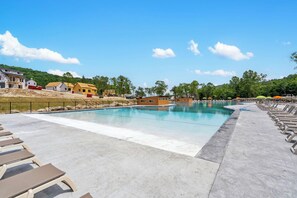 A swimming pool with lounge chairs and a small building, surrounded by trees and a clear sky.