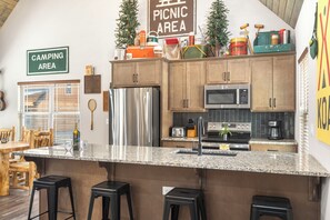 A kitchen with wooden cabinets, a stainless steel refrigerator, a microwave, and a bar area with stools.
