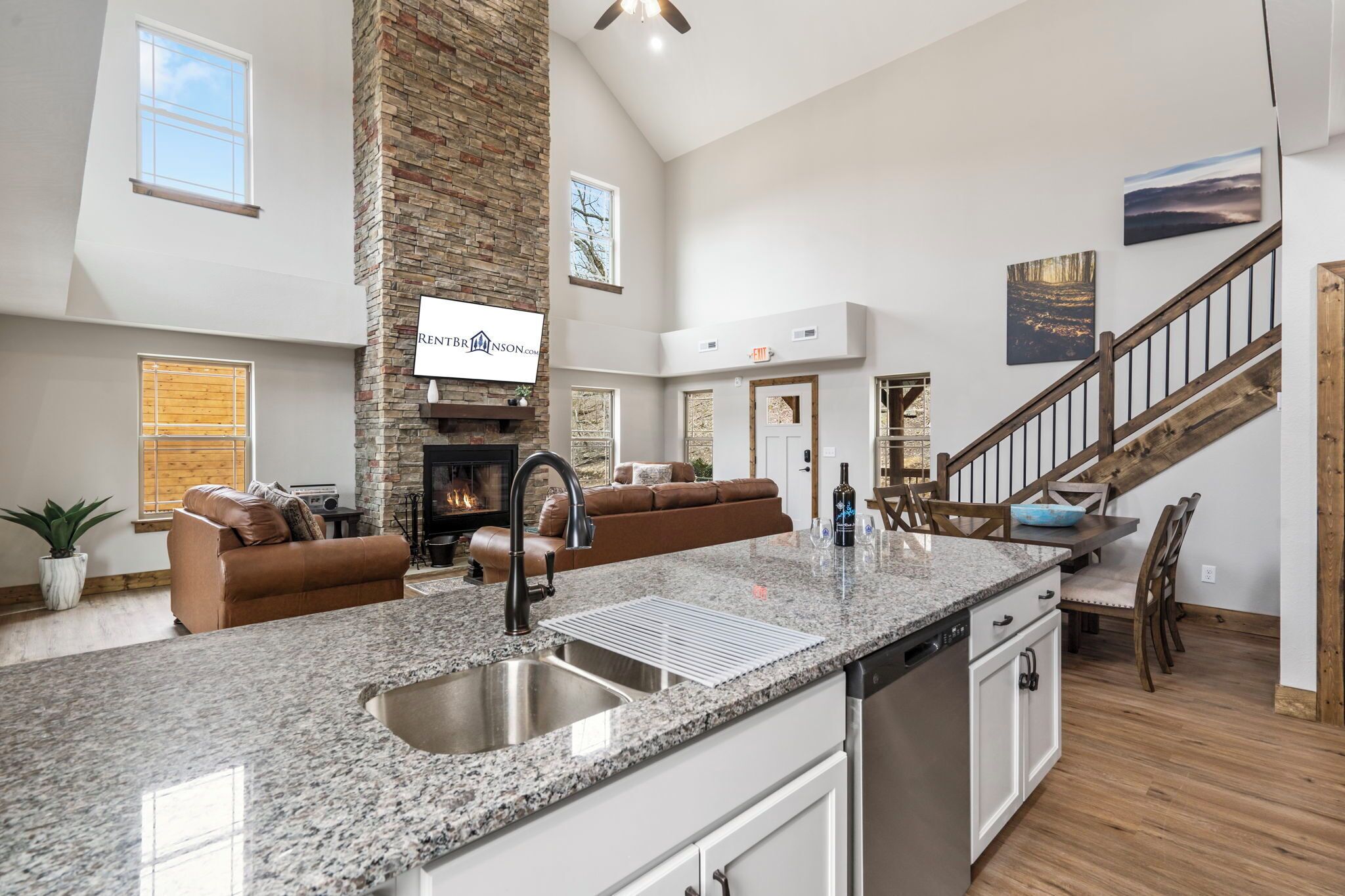 A spacious living area with a stone fireplace, a kitchen with granite countertops, and a staircase leading to upper floors.