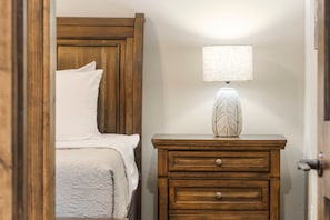 Quarto com cabeceira de madeira, mesa de cabeceira com abajur e cama com roupa de cama branca.