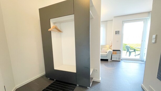 Un appartement moderne au design minimaliste, doté d’une armoire intégrée, d’un petit coin salon avec un canapé et d’un balcon aménagé avec du mobilier d’extérieur.
