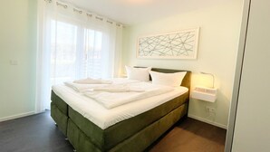 Un lit bien fait, avec du linge de lit blanc, une tête de lit verte et une œuvre d’art géométrique accrochée au mur au-dessus.