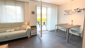 Un salon moderne comprenant un canapé, une table à manger et une porte-fenêtre coulissante donnant sur un espace extérieur.
