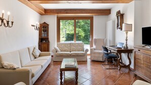 A living room with a sofa, a coffee table, a cabinet, a desk with a computer, and a large window. - Villa 'Ca' D'Ros Pool and Sauna' with Mountain View, Private Pool and Wi-Fi (Fontanile)