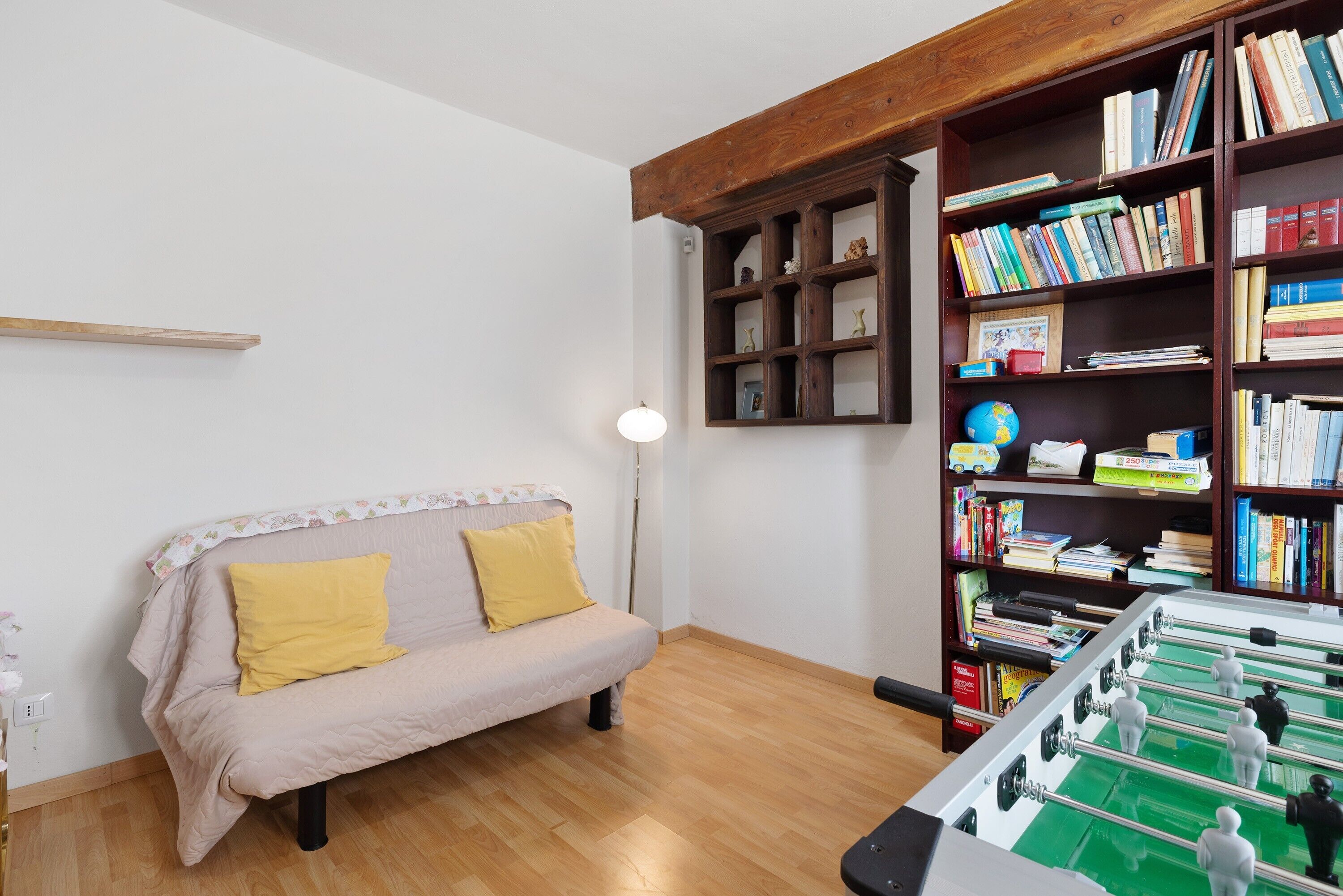 Una habitación con sofá, estantería y mesa de futbolín.