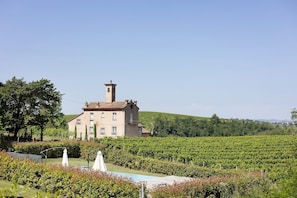Un grand bâtiment doté d’une tour, entouré d’un vignoble et d’un espace piscine.