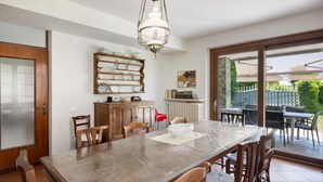 A dining area with a long table, chairs, a chandelier, a cabinet with dishes, and a view of the outside. - Villa 'Ca' D'Ros Pool and Sauna' with Mountain View, Private Pool and Wi-Fi (Fontanile)