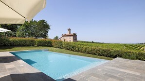 A swimming pool with stone tiles, a building with a tower, and a vineyard in the background. - Villa 'Ca' D'Ros Pool and Sauna' with Mountain View, Private Pool and Wi-Fi (Fontanile)