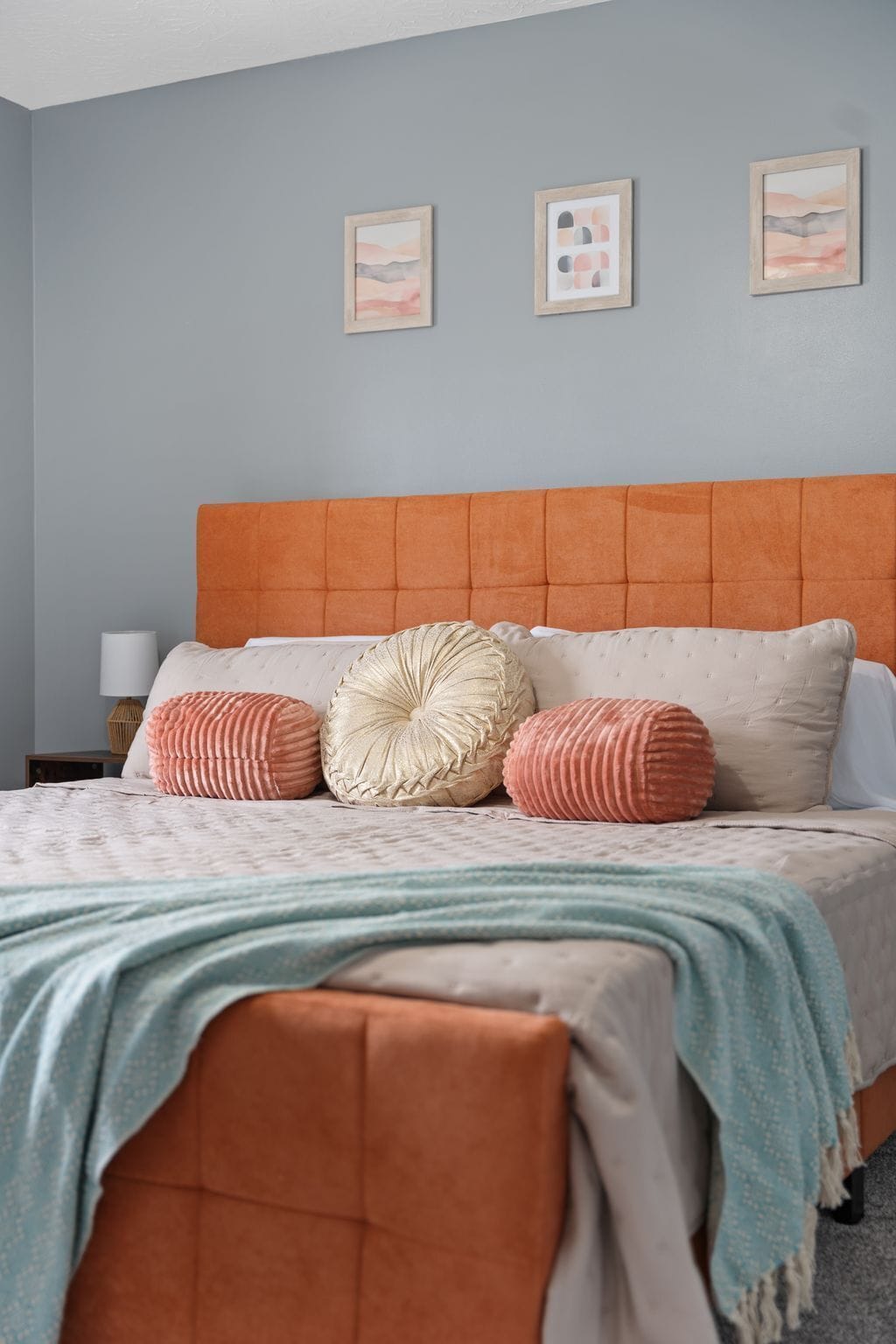 Un dormitorio con un cabecero naranja con botoneras, una cama con ropa de cama estampada y tres cuadros en la pared.