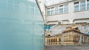 A building with a large mural of historical architecture, a wooden deck, and a glass facade reflecting the scene. - GuestReady - Ceuta Axis Awaits (Porto)