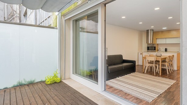 A modern kitchen with a dining area, a sliding glass door leading to a balcony, and a small seating area. - GuestReady - Ceuta Axis Awaits (Porto)