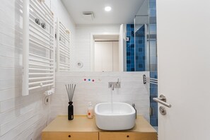 A modern bathroom with a white sink, a towel rack, a mirror, and a shower enclosure with blue tiles. - GuestReady - Lovely home in the city centre (Porto)