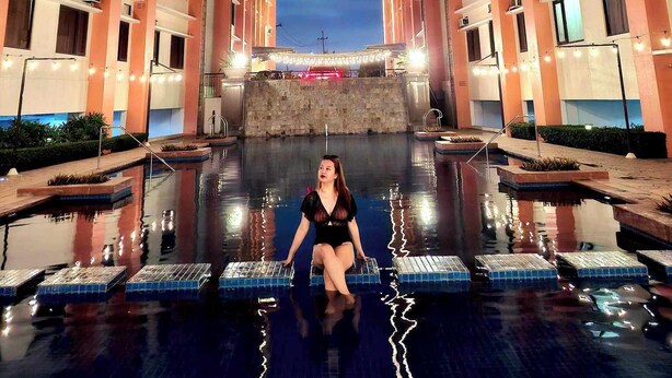 A person sitting on floating platforms in a swimming pool surrounded by high-rise buildings at night.