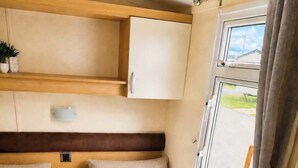 Un intérieur de camping-car compact comprenant un lit, une petite table, un placard et une fenêtre avec des rideaux.
