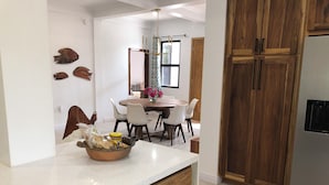 A modern kitchen with wooden cabinets, a stainless steel refrigerator, and a dining area with a round table and chairs.
