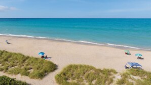 Una playa con agua turquesa cristalina, orilla de arena y dunas cubiertas de hierba.