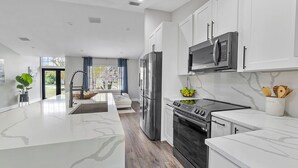 Una cocina moderna con armarios blancos, un refrigerador de acero inoxidable, un microondas y una estufa.