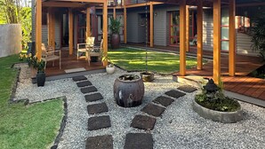 Ein modernes Haus mit überdachter Terrasse, Feuerstelle und Garten mit Kiesweg.