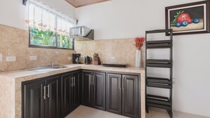 A kitchen with dark cabinets, a sink, a microwave, and a painting of fruits on the wall. - Rio Celeste Birds Garden apartment with A/C perfect for Family and couples (Upala)