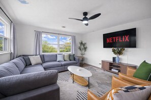 A modern living room with a grey sectional sofa, a coffee table, and a TV mounted on the wall displaying 'NETFLIX'.