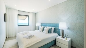 A modern hotel room with a large bed, a nightstand, a lamp, and a view of the sea through a window. - Sob O Mar II - Stunning beach/sea view (Armação de Pêra)