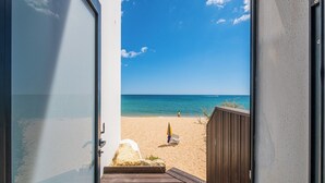 A beach view from a balcony with a wooden deck, a chair, and an umbrella. - Sob O Mar II - Stunning beach/sea view (Armação de Pêra)
