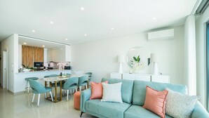 A modern living room with a teal sofa, a dining area with a glass table, and a kitchen in the background. - Sob O Mar III - Stunning beach/sea view (Armação de Pêra)