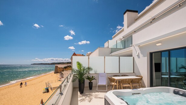 A balcony with a view of the beach, a hot tub, and a table with chairs. - Sob O Mar III - Stunning beach/sea view (Armação de Pêra)
