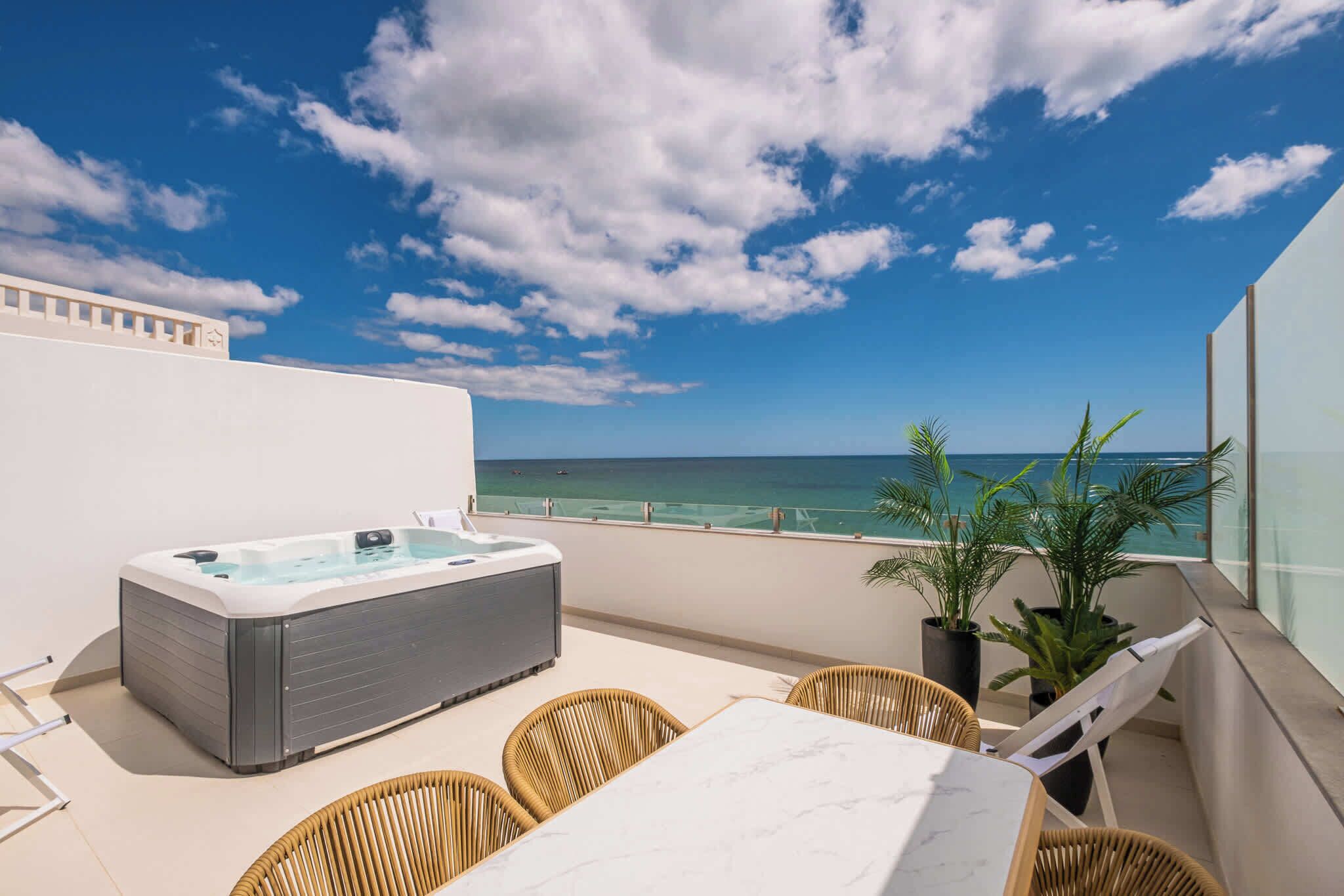 A rooftop terrace with a hot tub, wicker chairs, a table, and a view of the ocean.