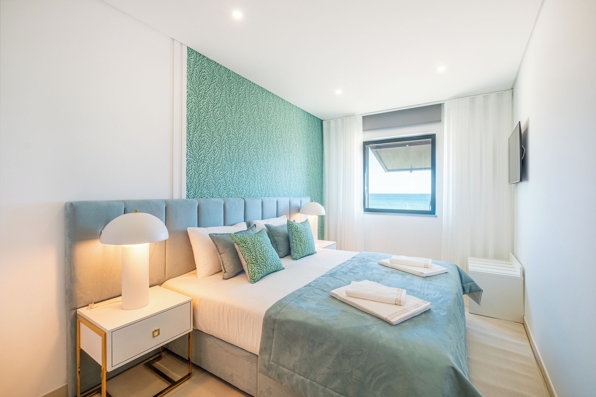 A modern hotel room with a large bed, a nightstand, and a window with curtains.