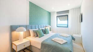 A modern hotel room with a large bed, a nightstand, and a window with curtains. - Sob O Mar III - Stunning beach/sea view (Armação de Pêra)