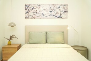 A bedroom with a bed, a nightstand, a lamp, and a painting on the wall.