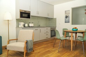 A modern kitchen with white cabinets, a microwave, and a stove. There is a dining area with a table and chairs.