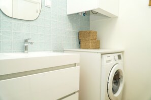 A modern bathroom with a white sink, a built-in washing machine, and wicker baskets on the countertop.