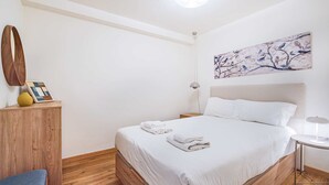 A hotel room with a large bed, a bedside table, a lamp, a wall art piece, and a wooden cabinet. - Stanchion Apartment (Albufeira)