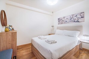 A hotel room with a large bed, a bedside table, a lamp, a wall art piece, and a wooden cabinet.