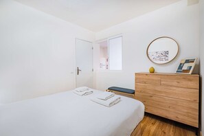 A bedroom with a bed, a wooden dresser, a window, and a wall-mounted artwork.