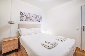 Une chambre à coucher avec un lit, une table de chevet, une lampe, un tableau et une porte.