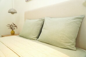 Sänky, jossa on kaksi tyynyä, yöpöytä maljakolla ja riippuvalaisin.