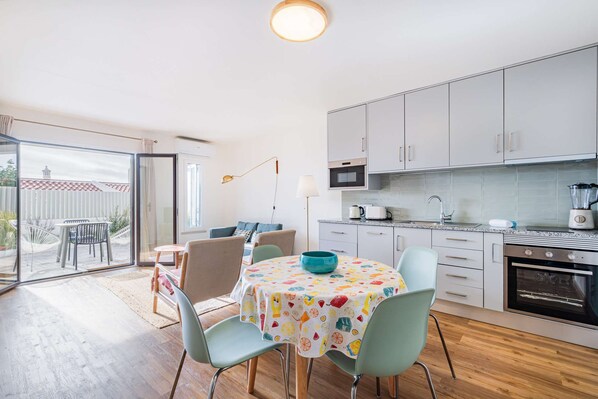A modern kitchen with white cabinets, a microwave, and a stove. There is a dining area with a table and chairs, and a large window providing a view of the outside.