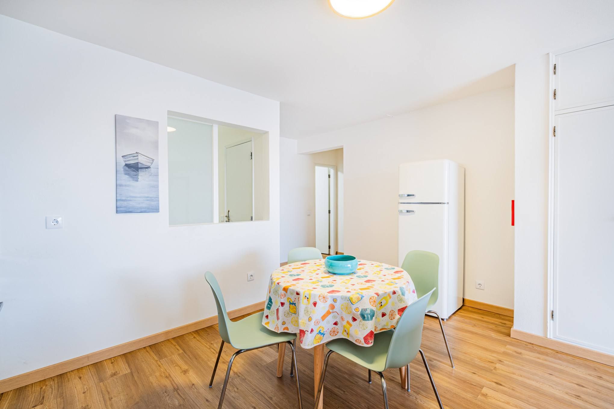 A small dining area with a table, chairs, a bowl, and a refrigerator.