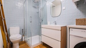 A bathroom with a toilet, a glass shower enclosure, a sink, and a washing machine. - Stanchion Apartment (Albufeira)