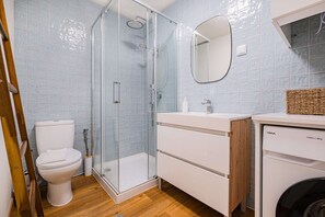 A bathroom with a toilet, a glass shower enclosure, a sink, and a washing machine.