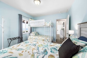 A room with a bunk bed, a desk, a chair, a mirror, and a window with a view.